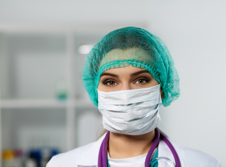 Female doctor's face wearing protective mask and green surgeon's cap closeup. Surgeon's eyes close up gazing intently in camera. Resuscitation concept.の写真素材