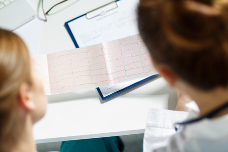 Two female doctors examining patient cardiogram chart. Professional conversation, council of cardiologists. Working conference. Medical conceptの写真素材