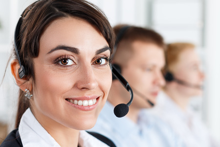 Three call center service operators at work. Portrait of smiling pretty female helpdesk employee with headset at workplace. Effective and efficient business information, help and support conceptの写真素材