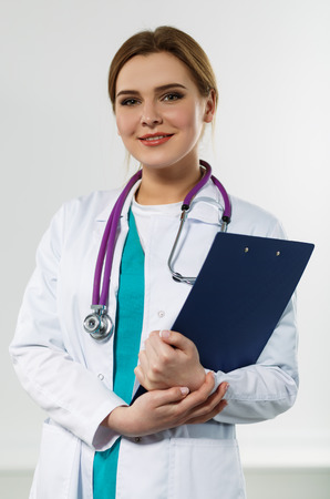 Beautiful smiling female medicine doctor holding clipped document pad. Medical help or insurance concept. Doctor is waiting for patient to examine. Physician reception conceptの写真素材