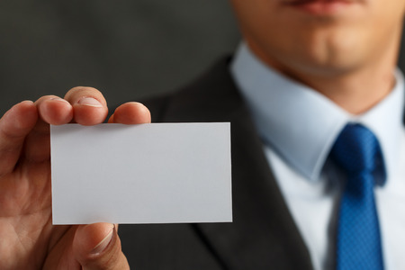 Businessman in suit and hand holding blank calling card. Male hand showing white visiting card in camera closeup. Partners contact information exchange concept. Introducing gesture at formal meetingの写真素材