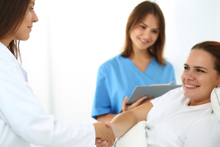 Female doctor shaking hands with patient lying in bed. Greeting and cheering gesture. Thankful handclasp for excellent treatment. Medical care or insurance concept. Physician ward roundの写真素材