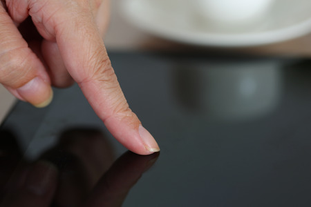 Female hand pointing in black tablet pc and using closeup it with cup of coffee in background.