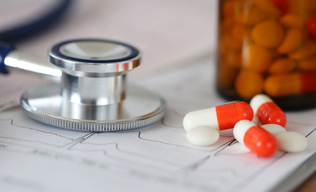 Medical stethoscope head lying on cardiogram chart with pile of pills closeupの写真素材
