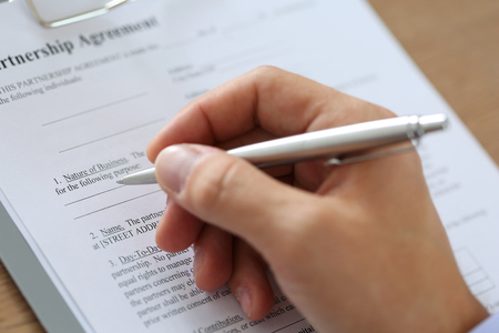 Hand of businessman in suit filling and signing with silver pen partnership agreement form clipped to pad closeup.の写真素材
