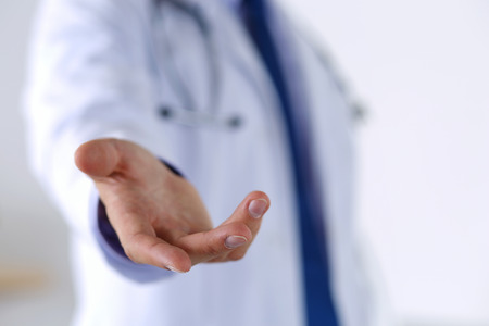 Male medicine doctor offering helping hand in office closeup. Friendly and cheerful gesture. Medical cure and tests advertisement concept. Physician ready to examine and save patientの写真素材