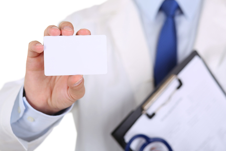 Male medicine doctor hand holding blank calling card. Physician showing white visiting card in camera closeup. Contact information exchange concept. Introducing gesture at formal meetingの写真素材