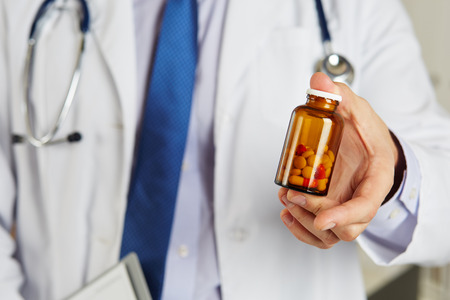Male medicine doctor hand holding and offering to patient jar of pills. Medical care, prescription, pharmacology, insurance concept. Giving or showing medications to patient. Physician ready to helpの写真素材