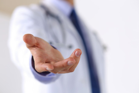 Male medicine doctor offering helping hand in office closeup. Friendly and cheerful gesture. Medical cure and tests advertisement concept. Physician ready to examine and save patient Male medicine doctor offering helping hand in office closeup. Friendly and cheerful gesture. Medical cure and tests advertisement concept. Physician ready to examine and save patient