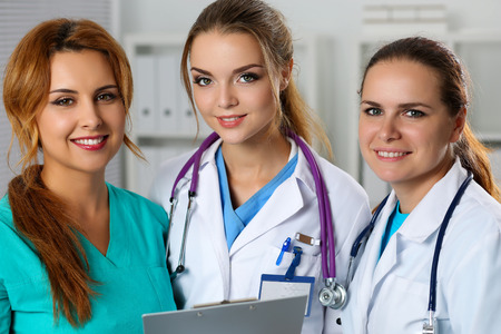 Three smiling female medicine doctors in office looking in camera portrait. Professional conversation, council or conference of physicians. Medical help, insurance, education, career conceptの写真素材