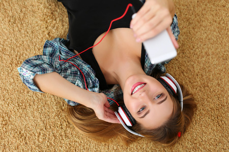 Beautiful blonde smiling woman lying on carpet floor wearing headphones.の写真素材