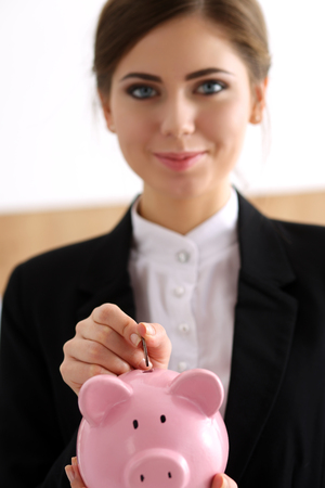 Hand of happy smiling businesswoman putting pin money into pink pig. Future needs loan, education or mortgage credit, spend vacation of dream, effective buying, financial risk and safety conceptの写真素材
