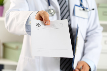 Male medicine doctor hand hold clipboard pad and give prescription to patient closeup. Panacea and life save, prescribe treatment, legal drug store, contraception concept. Empty form ready to be usedの写真素材
