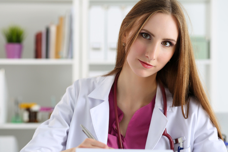 Beautiful smiling female doctor hold clipboard pad writing something. Physical, exam, er, disease prevention, ward round, patient visit check, 911, prescribe remedy, healthy lifestyle conceptの写真素材