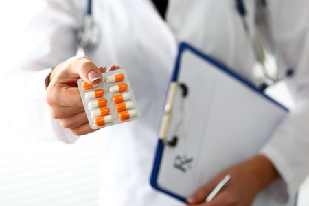 Female doctor hand hold prescription on clipboard pad and offer to patient tablet blister. Panacea, life save service, prescribe medicament, legal drug store, disease healing, blood pressure conceptの写真素材