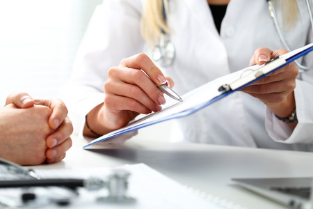Female doctor hand hold silver pen filling patient history list at clipboard pad. Physical, exam, er, disease prevention, ward round, visit check, 911, prescribe remedy, healthy lifestyle conceptの写真素材