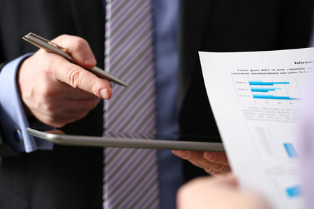 Businessmen and woman look and study statistics on electronic pad display closeup. Male arm opponent with silver pen point out problem collaboration coach cooperation partnership palm conceptの写真素材