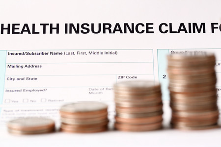 Pile of silver coins stand in front of health insurance form closeupの写真素材