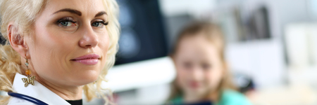Letterbox view of mature blonde doctor at her office receiving little patient filling in some medical form on clipboard pad portraitの写真素材