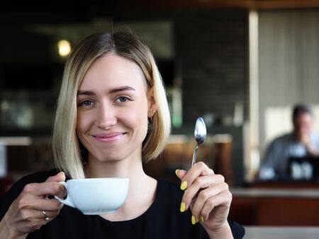 Beautiful smiling blonde woman drinking coffee and looking in camera headshotの写真素材