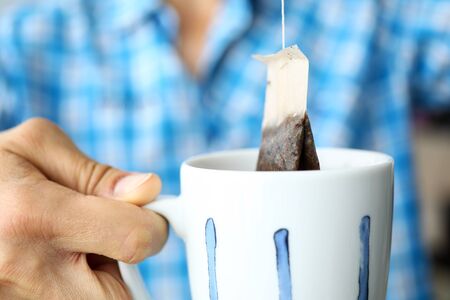 Man in blue shirt making cup of tea using modern handy teabag close-up