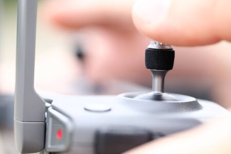 Male hand holding modern flying drone remote navigating it with stick macro