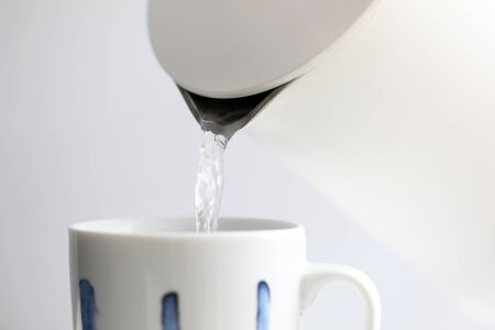 Boiling water trickling in white cup from kettle closeupの写真素材
