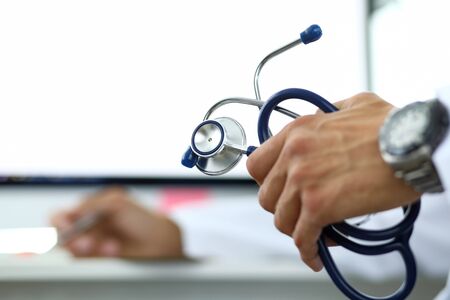 GP holding in hand stethoscope and writing something in background at working table close-upの写真素材