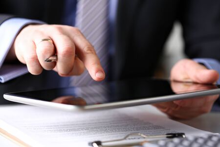 Male arm in suit and tie use silver pen and tablet pc close-up. Stock market statistic student read news via web or modern electronic bank assistance technology conceptの写真素材