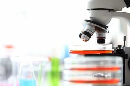 Microscope standing in school chemistry lab among bottles and flasks with colorful liquids closeup