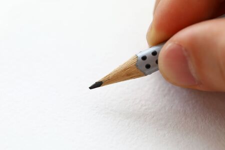 Male hand holding simple pencil ready to draw something on white paper macroの写真素材