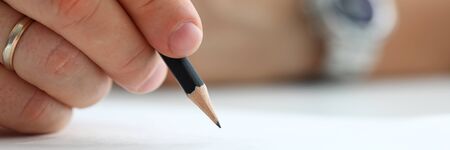 Letterbox view of male arm holding black simple pencil ready to draw something on white paper macro