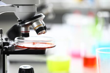 Microscope standing in school chemistry lab among bottles and flasks with colorful liquids closeup