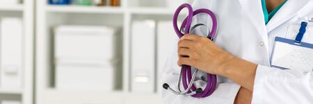 Beautiful smiling female doctor holding stethoscope with hands crossed on her chest. Medical help or insurance concept. Doctor is waiting for patient to examineの写真素材