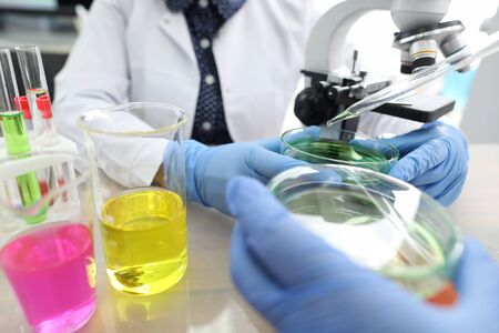 Close-up of two colleagues working on mutual experiment with liquid in flasks. Colourful substances...