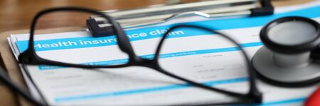 Close-up of health insurance application form lying on working table. Glasses and medical stethoscope. Healthcare concept. Letterbox viewの写真素材
