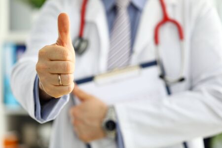 Male medicine doctor holding document pad in hand showing OK or approval sign with thumb up. High level and quality medical service best treatment healthy patient concept. Satisfied happy internの写真素材