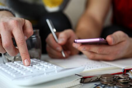 Close-up of couple with calculator and mobile phone planning budget at home. Bunch of coins on table...