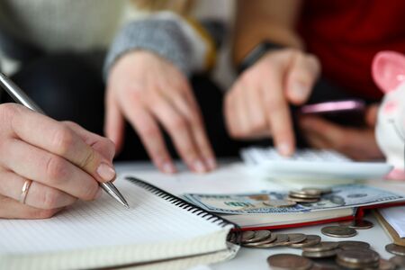 Close-up of spouse writing down all purchases and expenses in month. Couple counting income and saving-up. Banknotes and coins on table. Family bank and finance conceptの写真素材