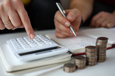 Close-up view of partners calculating expenses. Man writing down financial report. Stacks of coins on table. Family budget and economy problems conceptの写真素材