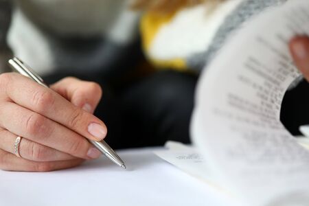 Close-up view of womans hand holding silver pen and writing in family budget notebook. Macro shot of female and attached checks. Finance planning conceptの写真素材