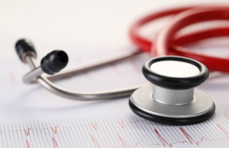 Close-up of red stethoscope and results of electrocardiogram on table. Heart diagnostic and general check-up of health. Medicine and cardiology conceptの写真素材