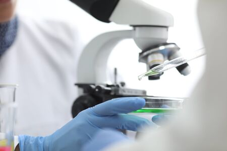 Close-up of chemists hands making experiment. Green substance dripping out of eyedropper on glass...
