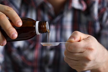 Close-up view of middle-aged mans hand pouring syrup in plastic spoon. Medicaion from signs of illness. Healthcare and low immunological protection conceptの写真素材