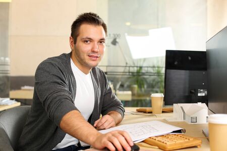 Portrait of young manager sitting at workplace and looking at camera with gladness. Handsome...