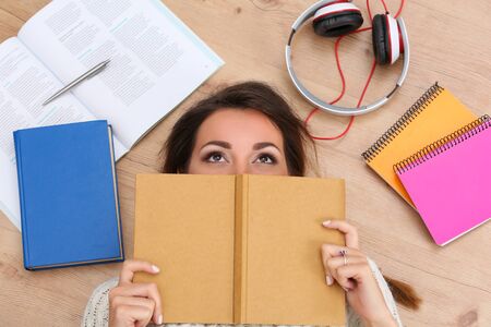 Top view of beautiful woman reading interesting book. Brunette lying on floor and covering face with notebook. Successful education and self development conceptの写真素材