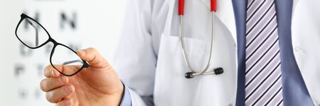 Male medicine doctor hands giving pair of black glasses to patient. Eyesight test and correction excellent vision laser surgery alternative driver health certificate examination conceptの写真素材
