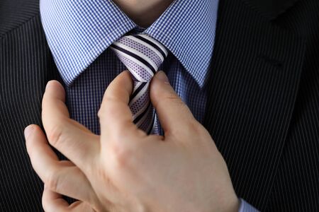 Close-up view of man straightens striped tie. Macro shot of corporate male in stylish suit adjusting necktie. Getting ready for business meeting conceptの写真素材
