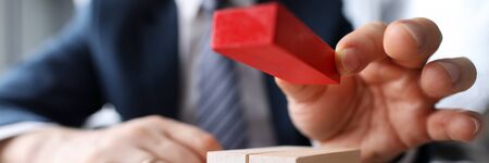 Close-up view of businessmans hand putting red block on small bunch of other bricks. Office worker...
