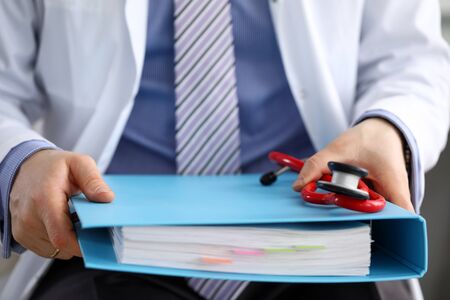 GP sitting in office holding in hands big binder with some important documents close-upの写真素材